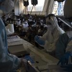 MSF Volunteers collect COVID tests as migrants sit on the floor in masks