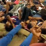 Men and boys lie on the ground in close quarters