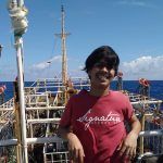 Crew member with red t-shirt leans against railing overlooking deck smiling, via Ferdi Arnando Facebook, July 7, 2021
