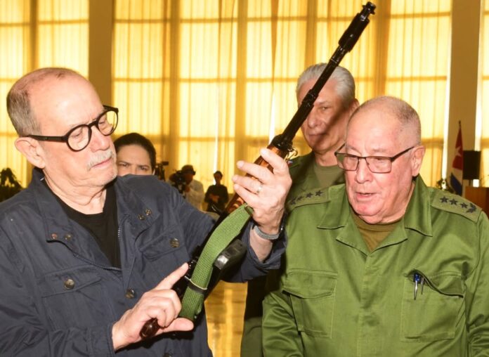 Silvio Rodriguez recibiendo un fusil AKM de manos del ministro de las Fuerzas Armadas, Álvaro López Miera; detrás, el mandatario Miguel Díaz-Canel